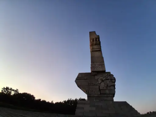 Pomnik Obrońców Wybrzeża na Westerplatte w Gdańsku, majestatyczny symbol bohaterstwa, na tle błękitnego nieba o zmierzchu.