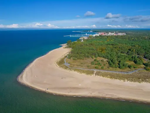 Piękna plaża i las na Helu. W oddali widać miasteczko i port, idealne miejsce na wakacyjne atrakcje.