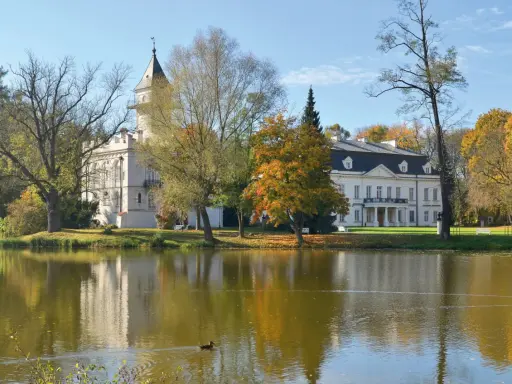 Pałac w Bolimowskim Parku Krajobrazowym odbija się w spokojnej tafli jeziora, otoczony jesiennymi drzewami.