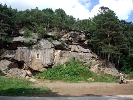 Skalny krajobraz w Polsce, z imponującymi formacjami skalnymi porośniętymi lasem sosnowym. Na skale widoczna tablica pamiątkowa.