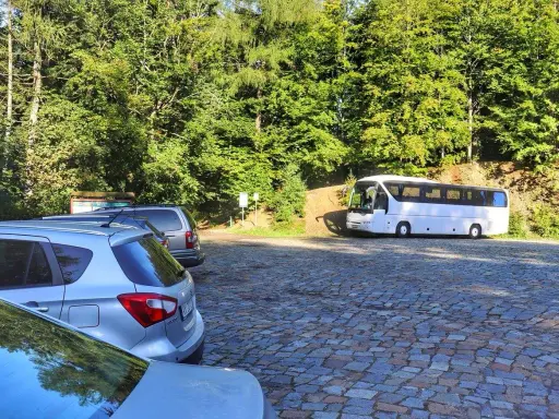 Parking na czupel trasie. Biały autokar i samochody na brukowanym placu wśród zieleni.