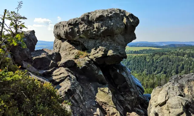 Wielkie, szare skały górują nad zieloną doliną. W oddali widać białe skały i pagórki.