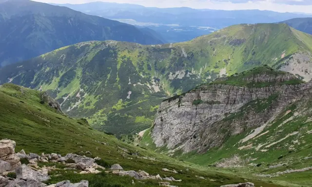 Malownicza trasa w Kościelisku. Zielone zbocza górskie, skaliste urwisko i pasma górskie w oddali tworzą zapierający dech w piersiach krajobraz.