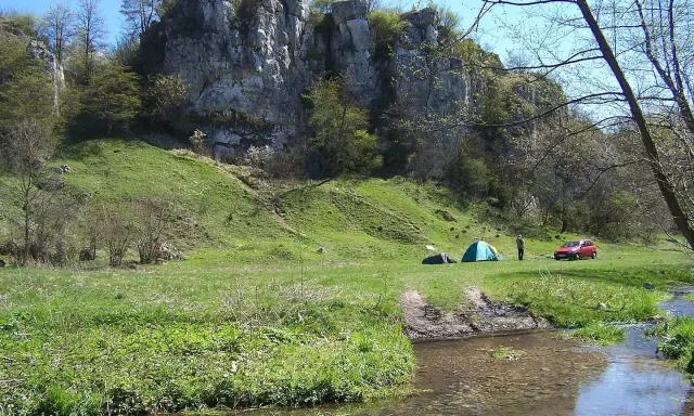 Malownicza dolina Kluczwody z rozbitymi namiotami, czerwonym samochodem i strumieniem. Skaliste zbocza porośnięte zielenią.