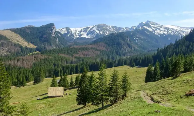 Piękne trasy Tatry. Zielone hale, lasy i ośnieżone szczyty. Drewniana chata i ścieżka zapraszają do wędrówki.