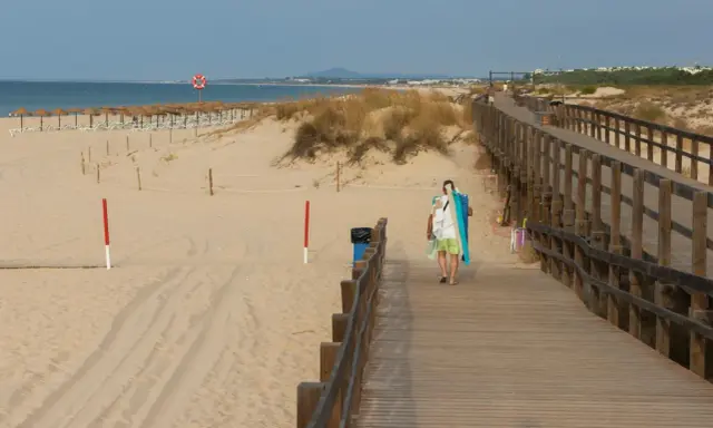 Spacer plaży z drewnianą kładką i osobą niosącą sprzęt plażowy. Grzybowo atrakcje czekają!