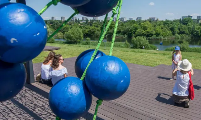 Tarnów atrakcje dla dzieci: dwie kobiety siedzą na drewnianym tarasie, a mała dziewczynka w letniej sukience i kapeluszu pozuje do zdjęcia.