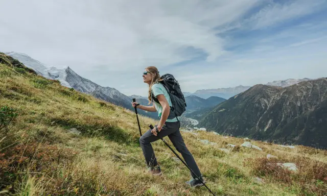 Kobieta z plecakiem i kijkami wspina się po zboczu. Widok gór i doliny. Zastanawia się, ile się idzie na Giewont.