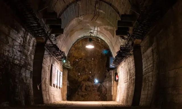 Wnętrze tunelu w Górach Sowich. Betonowe ściany, łukowe sklepienie i oświetlenie tworzą mroczny klimat.