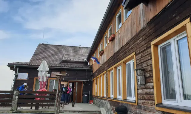 Drewniane schronisko w Górach Opawskich, z tarasem i schodami. W tle błękitne niebo z chmurami.