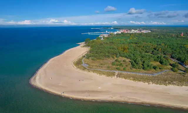 Piękna plaża i las na Helu. W oddali widać miasteczko i port, idealne miejsce na wakacyjne atrakcje.