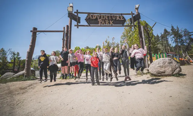 Radosna grupa dzieci skacze przed bramą "Adventure Park" w Gdyni.