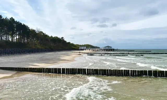 Plaża z drewnianymi falochronami i budynkami nad morzem, przypominająca najcieplejsze regiony Polski.