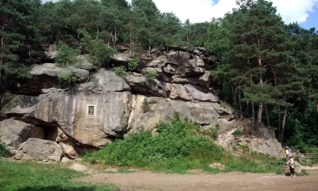 Skalny krajobraz w Polsce, z imponującymi formacjami skalnymi porośniętymi lasem sosnowym. Na skale widoczna tablica pamiątkowa.