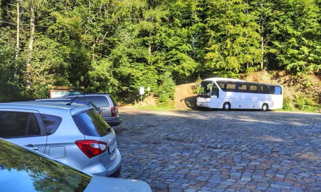 Parking na czupel trasie. Biały autokar i samochody na brukowanym placu wśród zieleni.