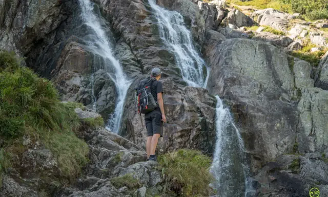Turysta podziwia wodospad na szlaku turystycznym w Tatrach Wysokich.