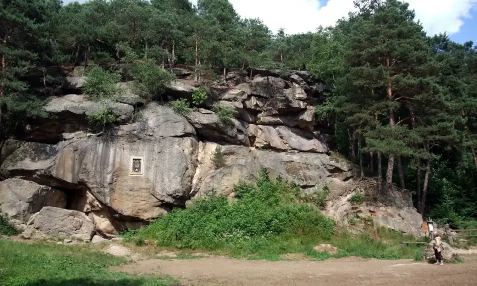 Skalny krajobraz w Polsce, z imponującymi formacjami skalnymi porośniętymi lasem sosnowym. Na skale widoczna tablica pamiątkowa.