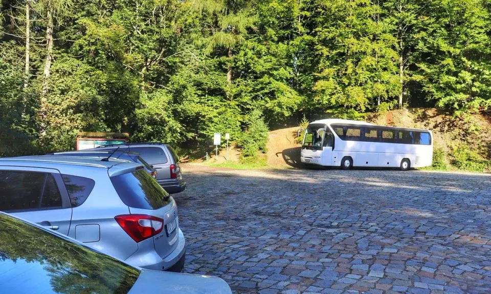 Parking na czupel trasie. Biały autokar i samochody na brukowanym placu wśród zieleni.