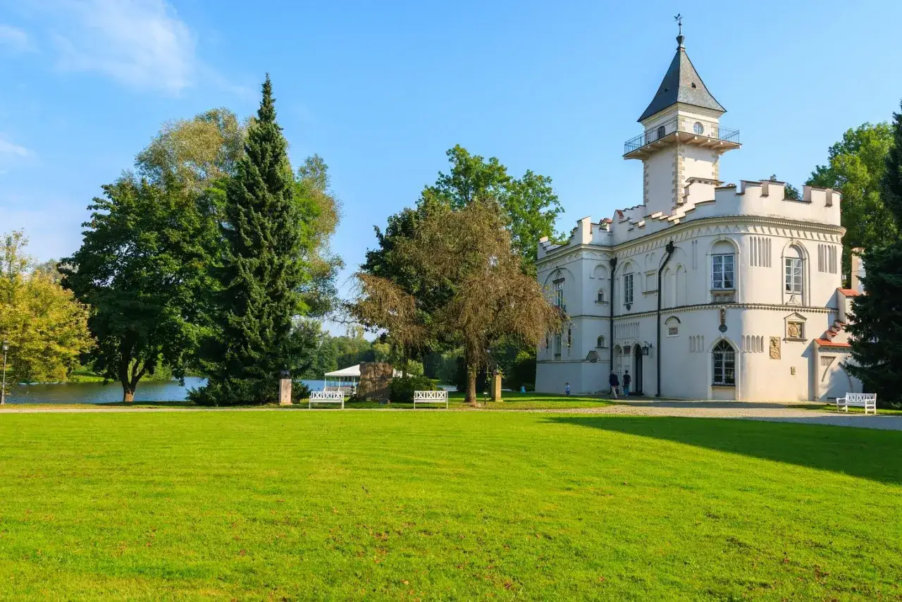 Biały pałac z wieżą, otoczony zielonym parkiem i jeziorem, to piękne atrakcje mazowieckie.