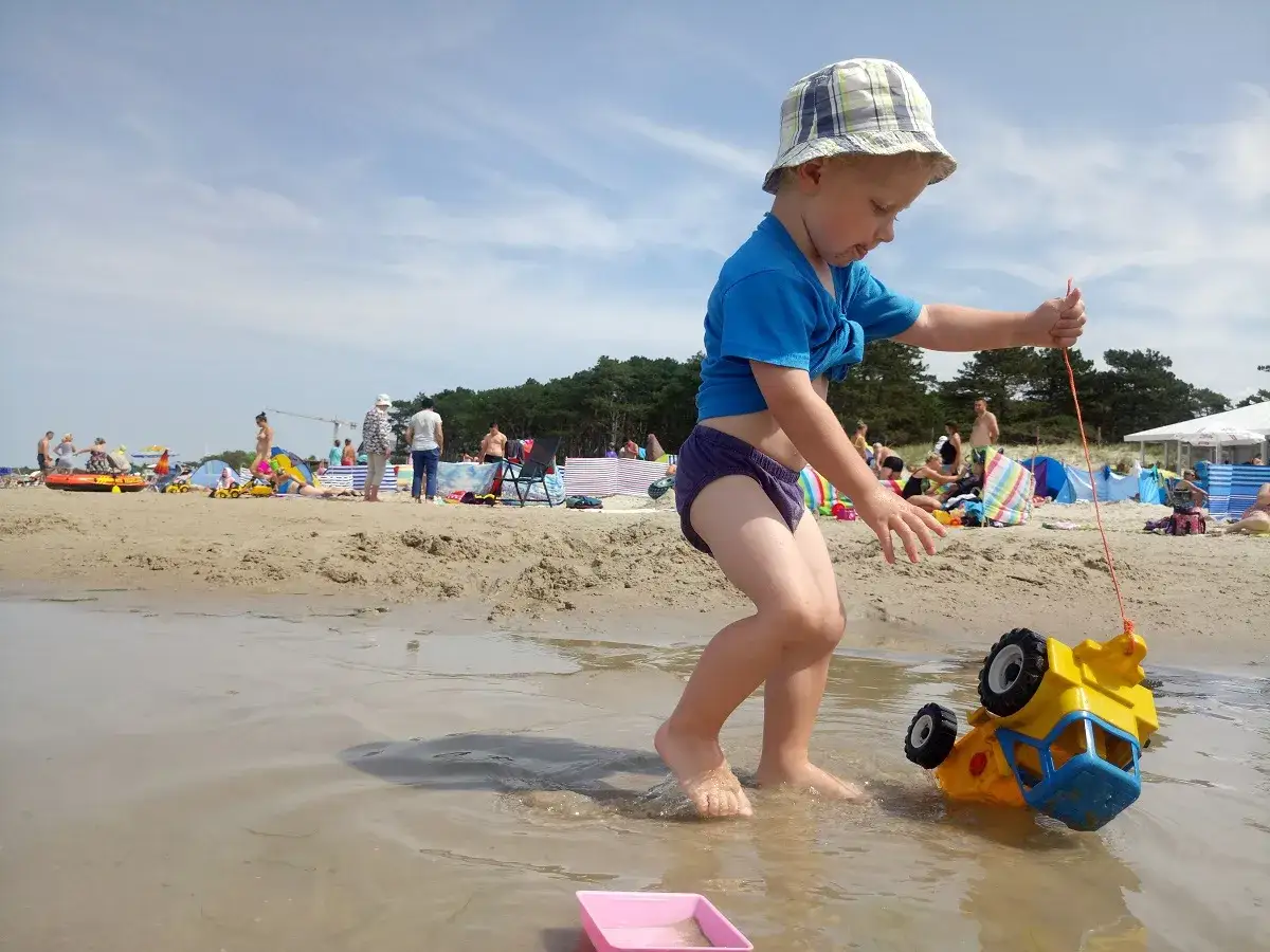 Chłopiec ciągnie zabawkowe auto na plaży w Darłowie. To świetne darłowo atrakcje dla dzieci.