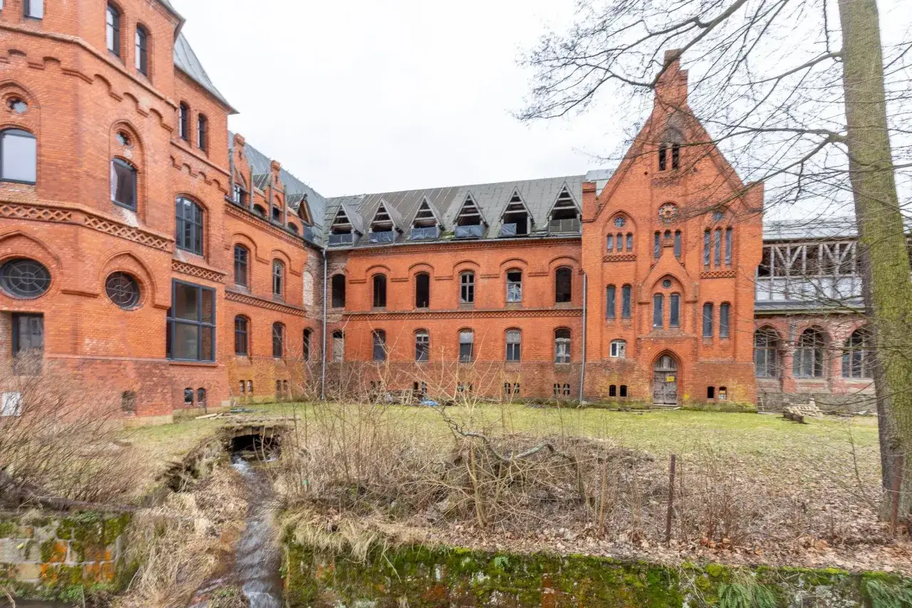 Sokołowsko atrakcje: opuszczony, ceglany budynek sanatorium z charakterystycznymi lukarnami i strumieniem.