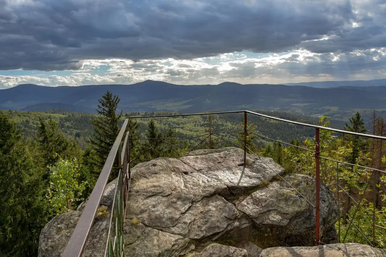 Widok z platformy widokowej na skalnym rumowisku. W oddali g&oacute;ry i lasy, nad nimi burzowe chmury. To idealne miejsce na podziwianie krajobraz&oacute;w, jak na punkcie widokowym Trojak w Lądku-Zdroju.