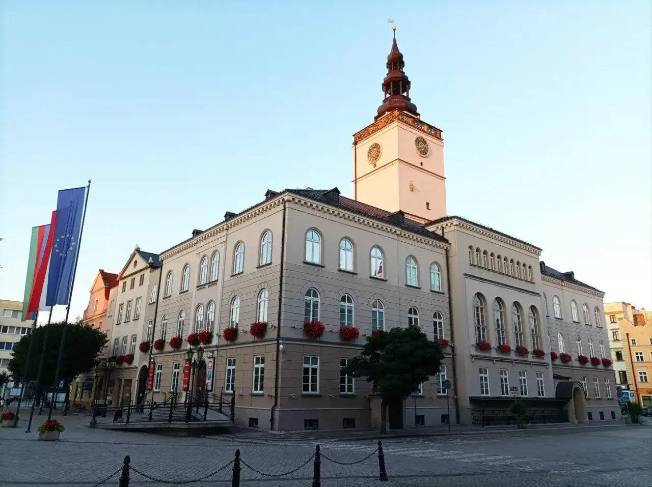 Ratusz w Dzierżoniowie, z charakterystyczną wieżą i zegarem, to jedna z głównych atrakcji miasta. Flagi UE i Polski dumnie powiewają przed budynkiem.