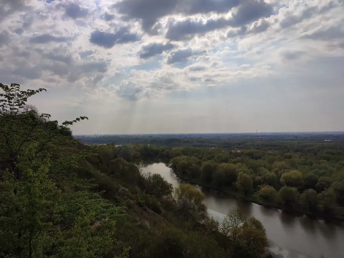 Widok z g&oacute;ry na meandrującą rzekę i las. Chmury na niebie tworzą wrażenie, jakby to były g&oacute;ry pieprzowe.