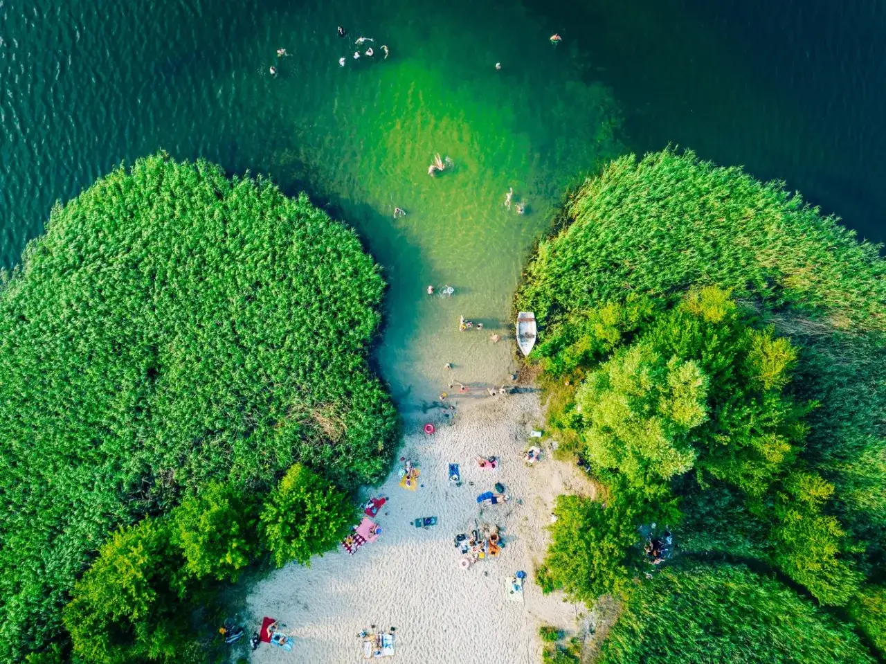 Wakacje nad najpiękniejszym jeziorem w Polsce. Ludzie kąpią się i opalają na piaszczystej plaży otoczonej zielenią.