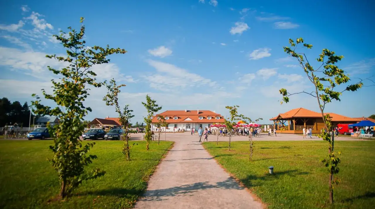 Teren rekreacyjny z budynkami, placem i alejkami. Widać ludzi, samochody i drzewa. To idealne miejsce na odkrywanie basznia dolna atrakcje.