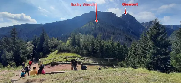 Widok na Suchy Wierch i Giewont z początku szlaku w Dolinie Strążyskiej. Turyści odpoczywają na ścieżce.