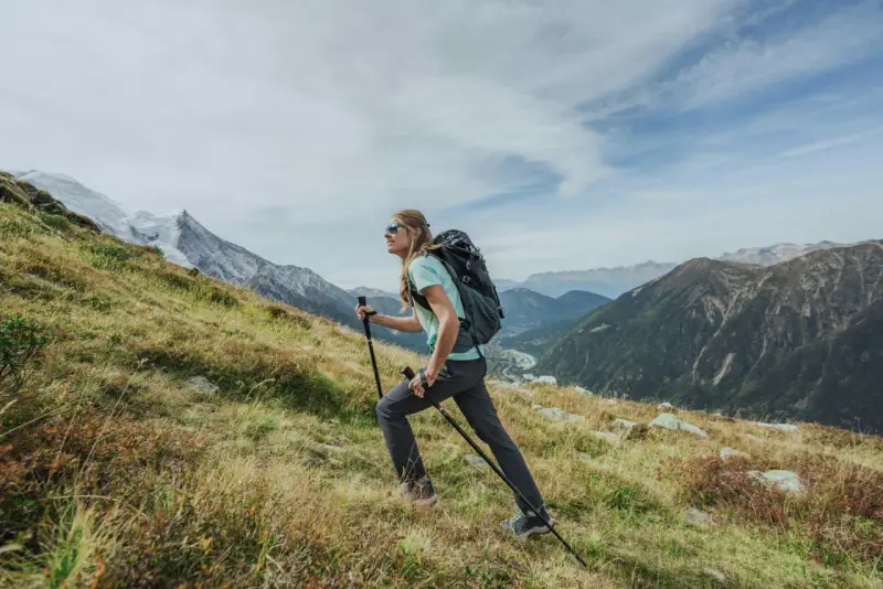Kobieta z plecakiem i kijkami wspina się po zboczu. Widok gór i doliny. Zastanawia się, ile się idzie na Giewont.