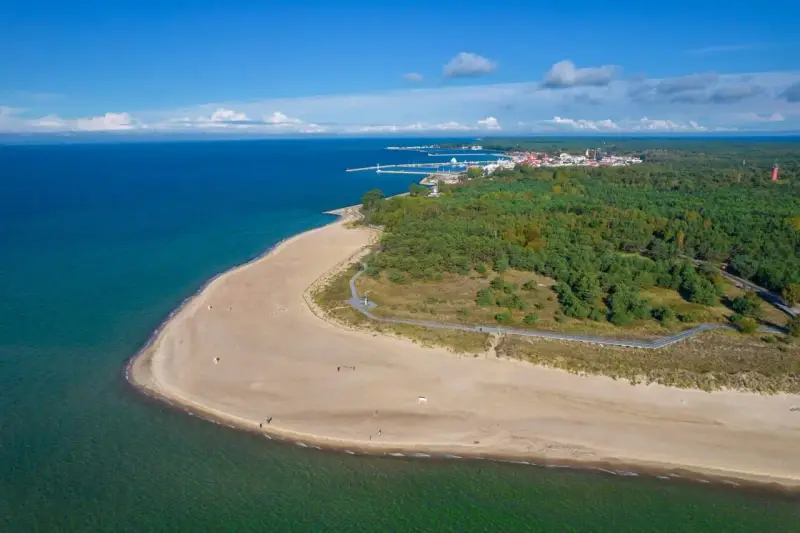 Piękna plaża i las na Helu. W oddali widać miasteczko i port, idealne miejsce na wakacyjne atrakcje.