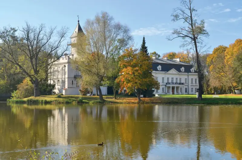 Pałac w Bolimowskim Parku Krajobrazowym odbija się w spokojnej tafli jeziora, otoczony jesiennymi drzewami.